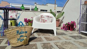A patio with a white chair, a wicker basket, and potted plants.