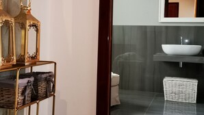 A modern bathroom with a large mirror, a white sink, and a gold-framed shelf with decorative items.