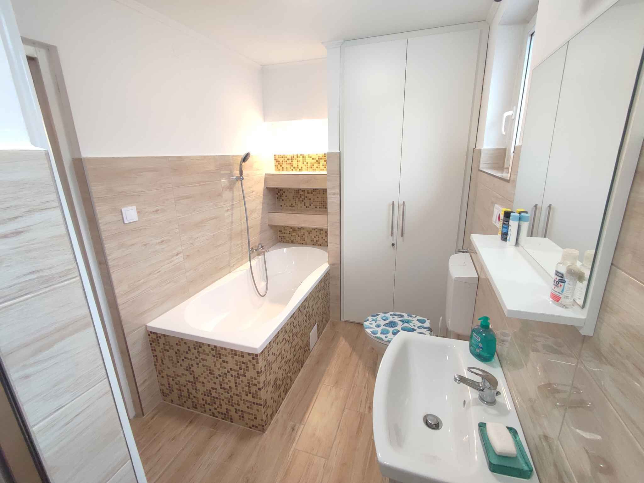 Ein Badezimmer mit einer Badewanne, einem Waschbecken und einer Toilette. Über dem Waschbecken befindet sich ein Spiegel und darunter ein Schrank mit Toilettenartikeln.