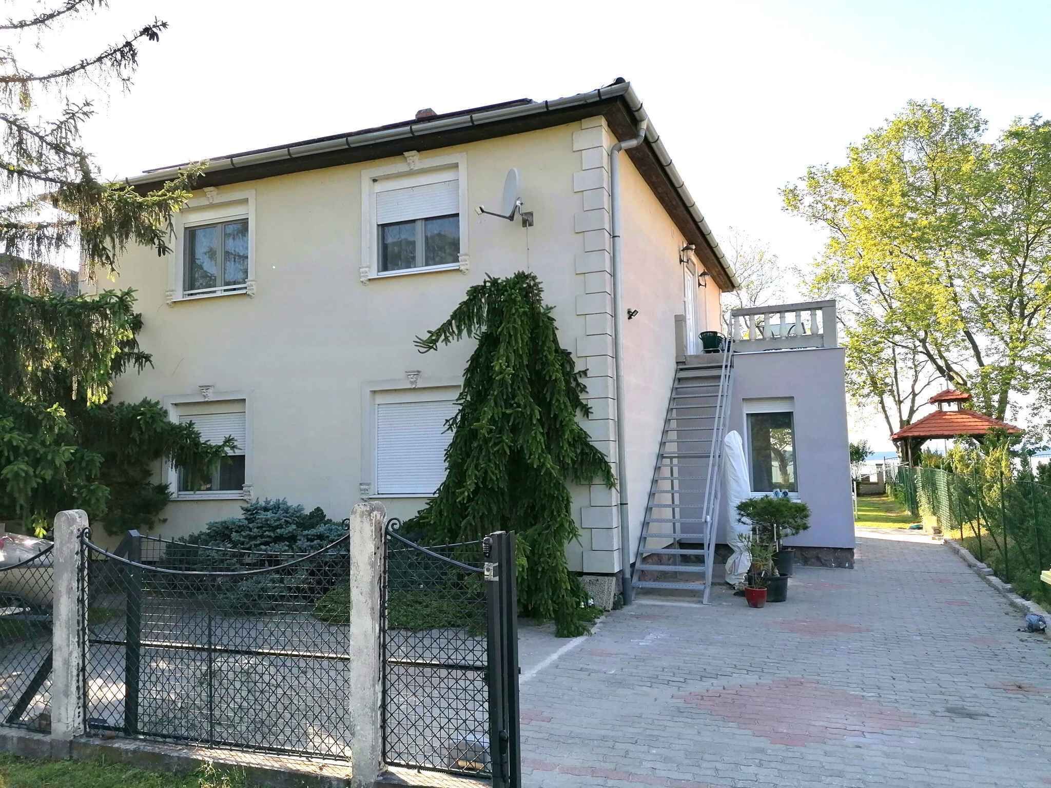 A two-story building with a gated entrance, a small outdoor area with a ladder, and a gazebo in the background.