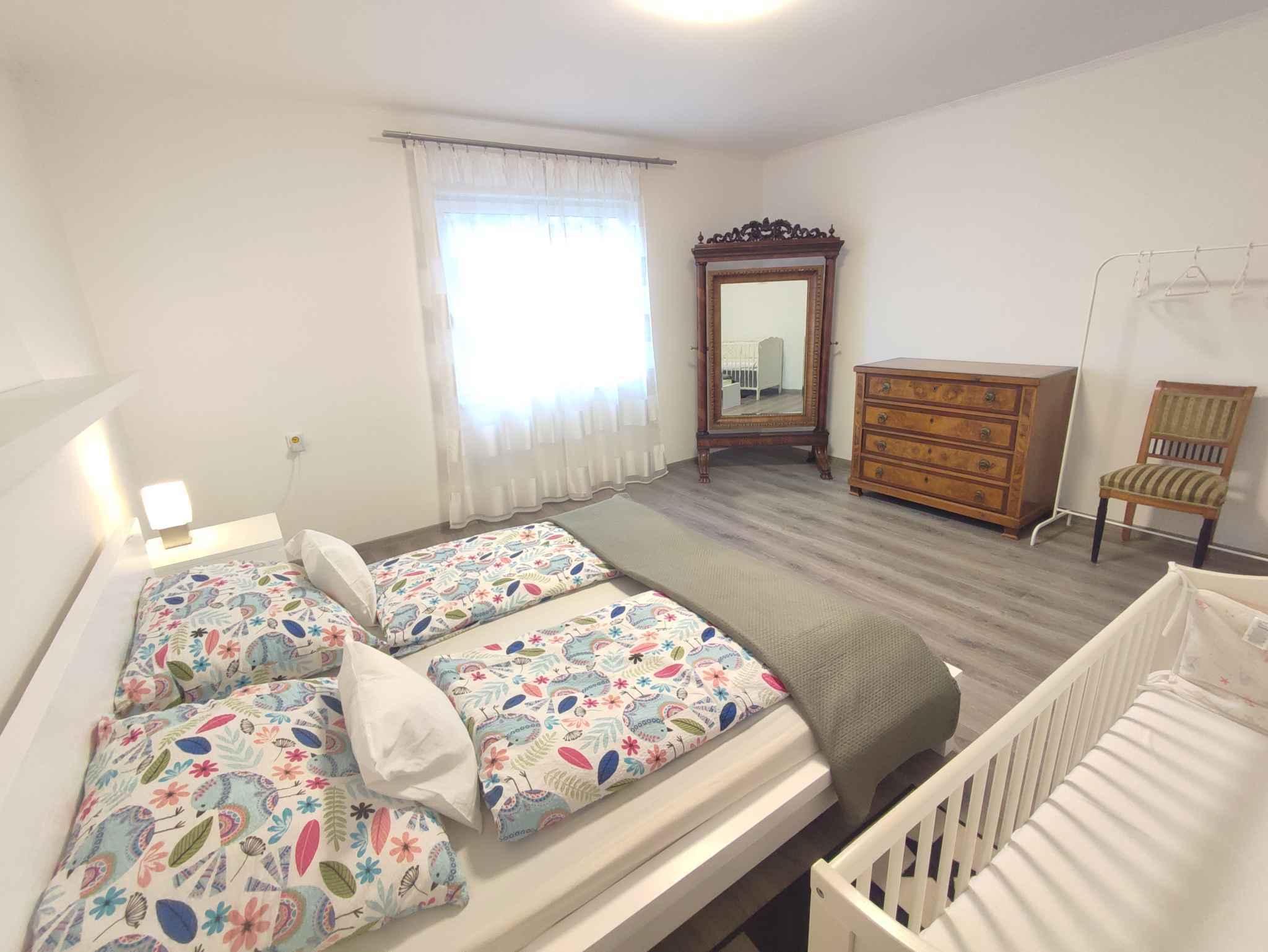 A bedroom with two beds, a dresser, a chair, a mirror, and a window with curtains.