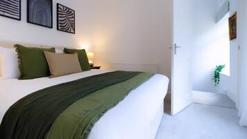 A bedroom with a bed, bedside tables, a nightstand, and wall art.