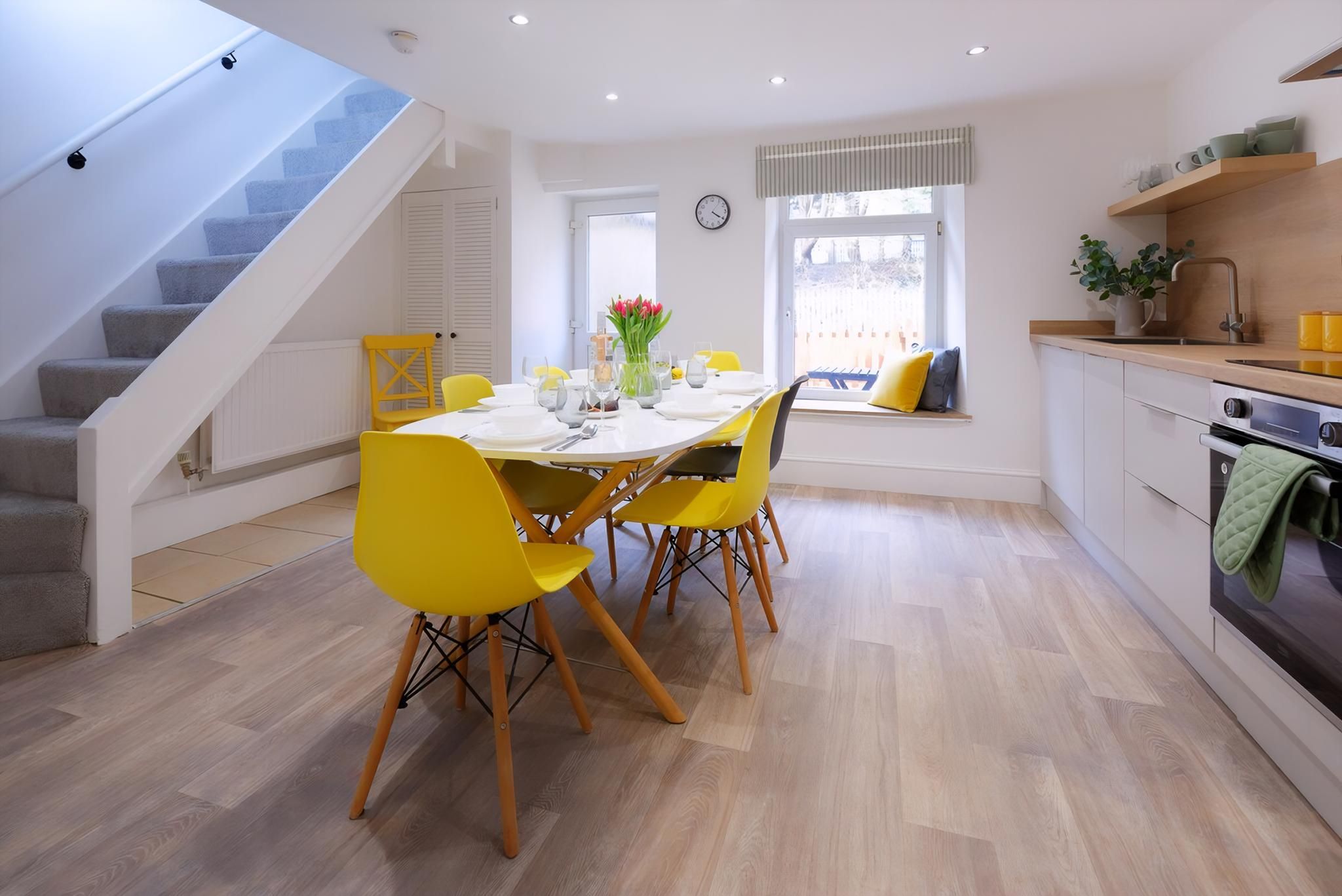 A modern kitchen with a dining area, wooden flooring, and a staircase.