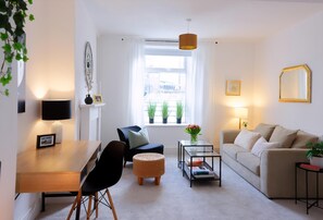 A modern living room with a dining area, a sofa, a coffee table, and a window with plants. - 3 Bed Home near Hiking Trails & Parks (Rhondda)