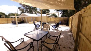 Een terras buiten met een tafel en stoelen, een overdekte zithoek en een houten omheining.