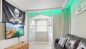Un salon avec un t éléviseur fixé au mur, un banc en bois, un canapé en cuir et une fenêtre avec des stores.