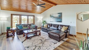 Un salón amplio con techo alto, vigas de madera, un ventanal grande y una chimenea.