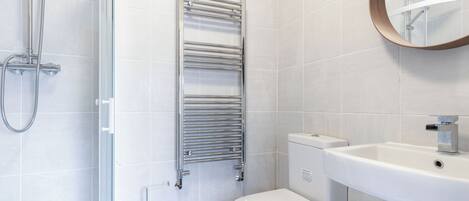Un bagno moderno con cabina doccia in vetro, portasci in cromo, vaso sanitario bianco e lavandino con specchio sopra.