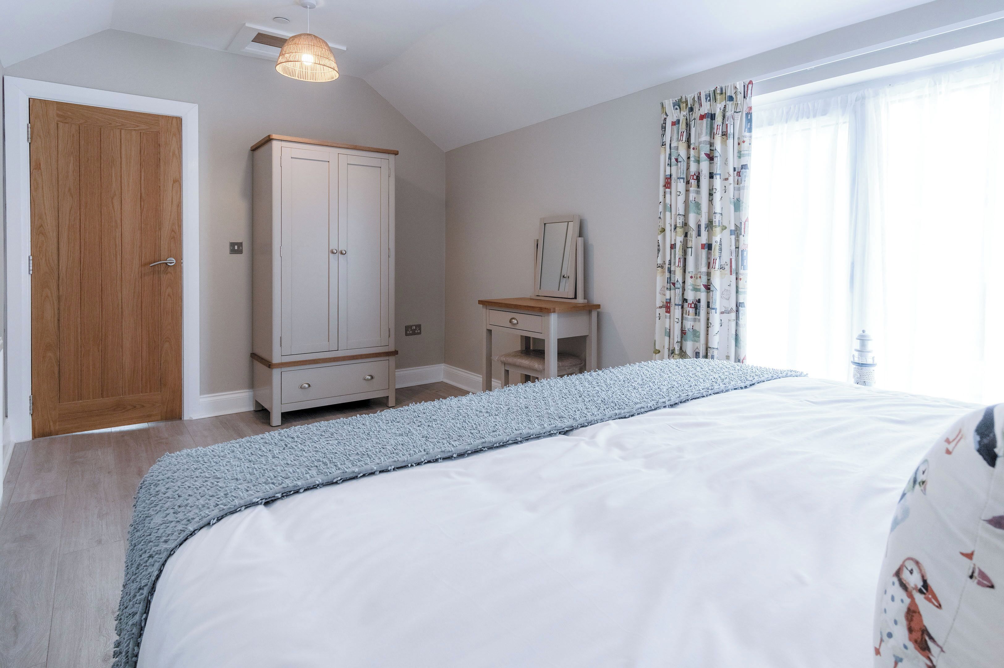 A bedroom with a bed, a wardrobe, a vanity with a mirror, and a window with curtains.