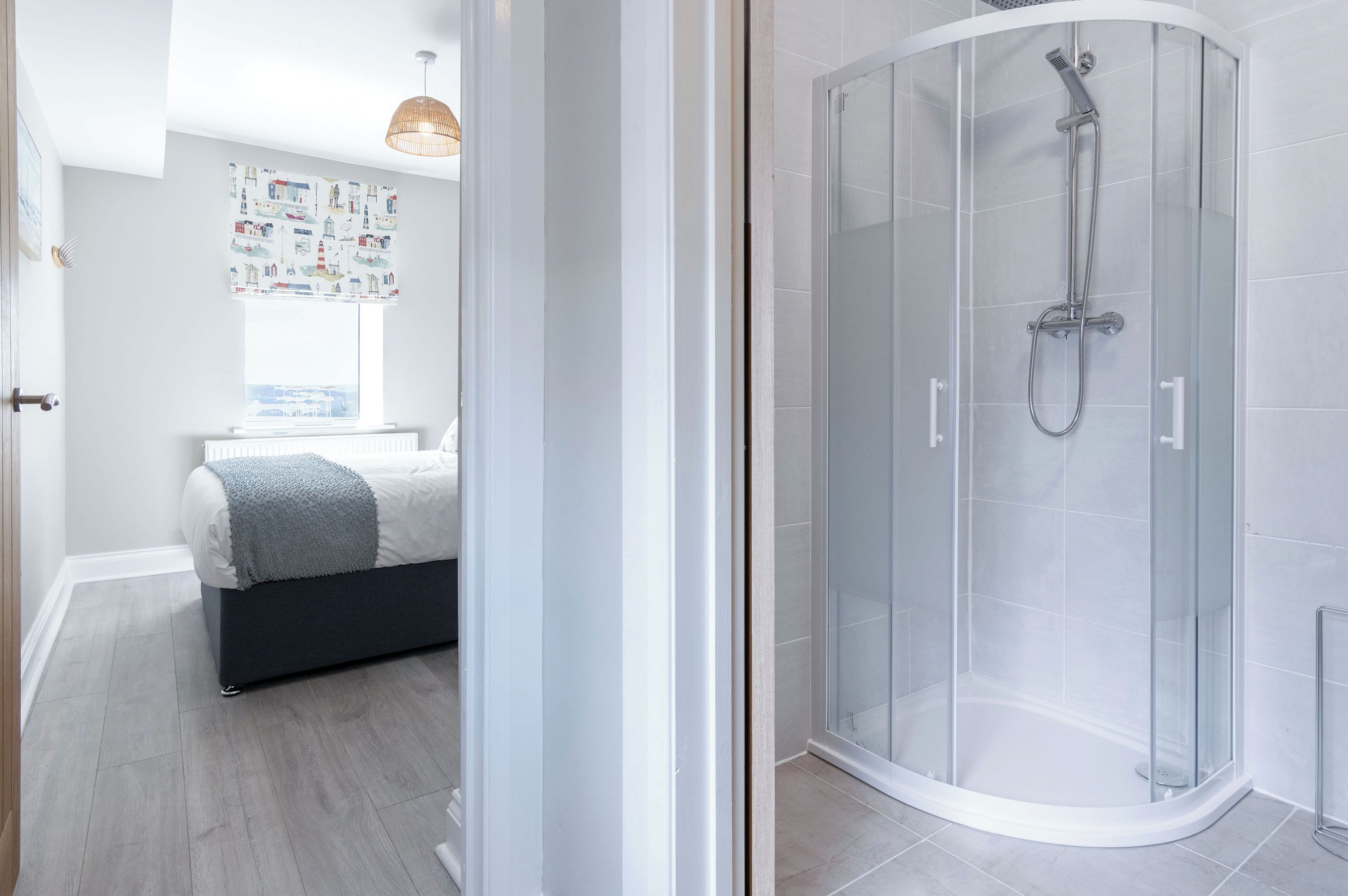 Ein modernes Badezimmer mit einer gläsernen Dusche, einem Bett mit grauer Decke und einem Fenster mit Blick auf die Stadt.