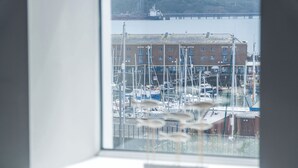 A marina with boats docked, a building in the background, and a window with a view of the marina. - Harbour View - 2 Bedroom Apartment - Milford Haven (Milford Haven)