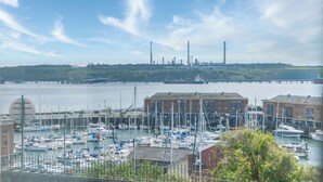A marina with boats docked, a bridge in the background, and industrial buildings on the opposite shore. - Harbour View - 2 Bedroom Apartment - Milford Haven (Milford Haven)