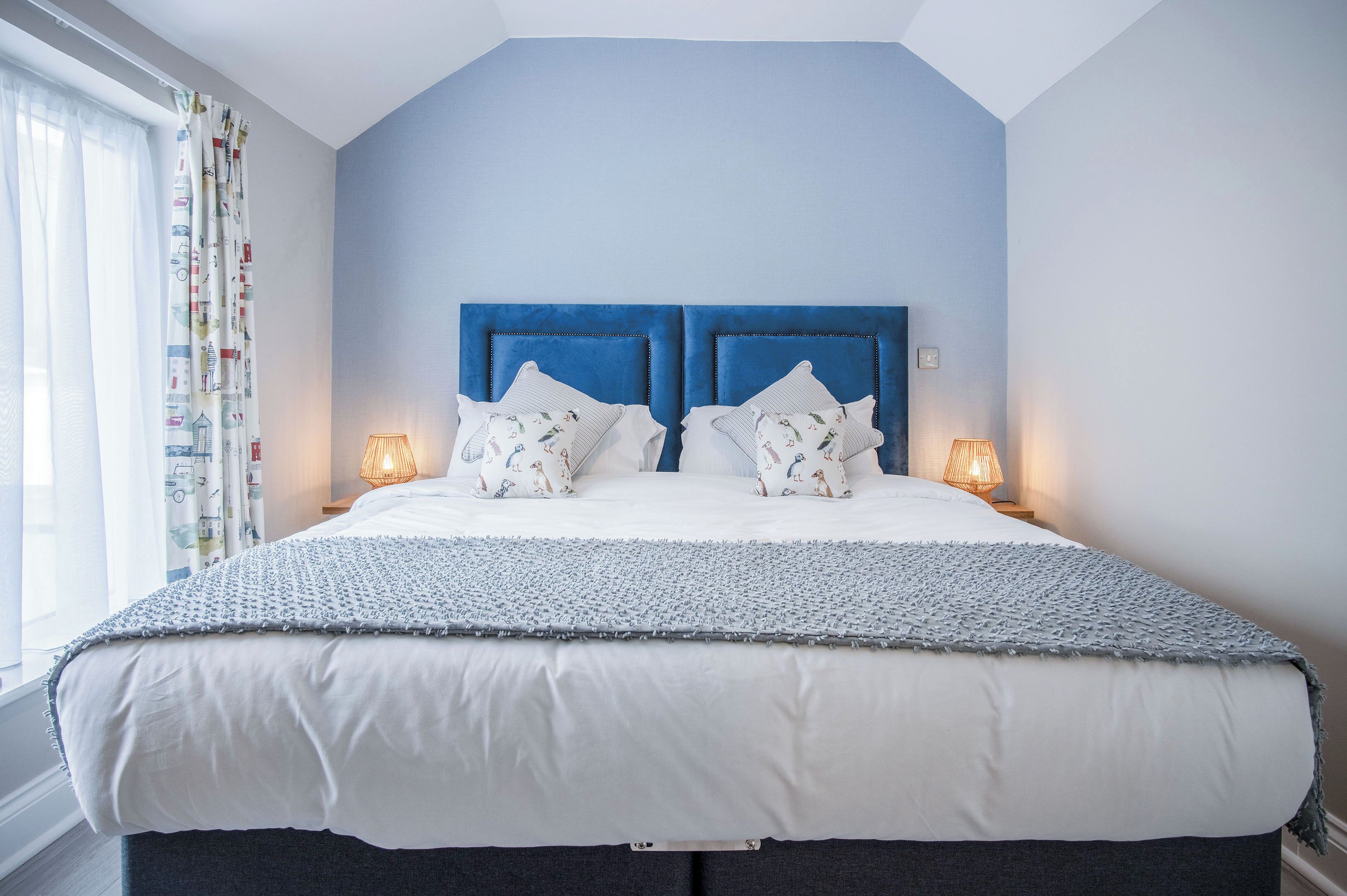 Un lit bien fait, avec une tête de lit bleue, du linge de lit blanc et deux lampes de chevet.
