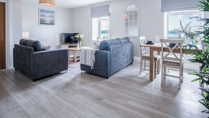 A modern living room with a sofa, TV, and dining area. - Haven View - 2 Bedroom Apartment - Milford Haven (Milford Haven)