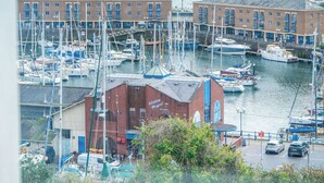 A marina with boats docked, a building labeled 'Marlborough Vineyard', and a parking area with cars. - Harbour Heights - 2 Bed Apartment - Milford Haven (Milford Haven)