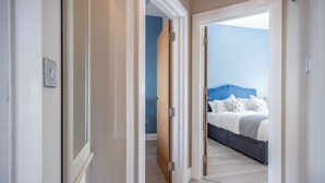 A hallway leading to a bedroom with a bed, a nightstand, and a dresser. - Harbour Heights - 2 Bed Apartment - Milford Haven (Milford Haven)