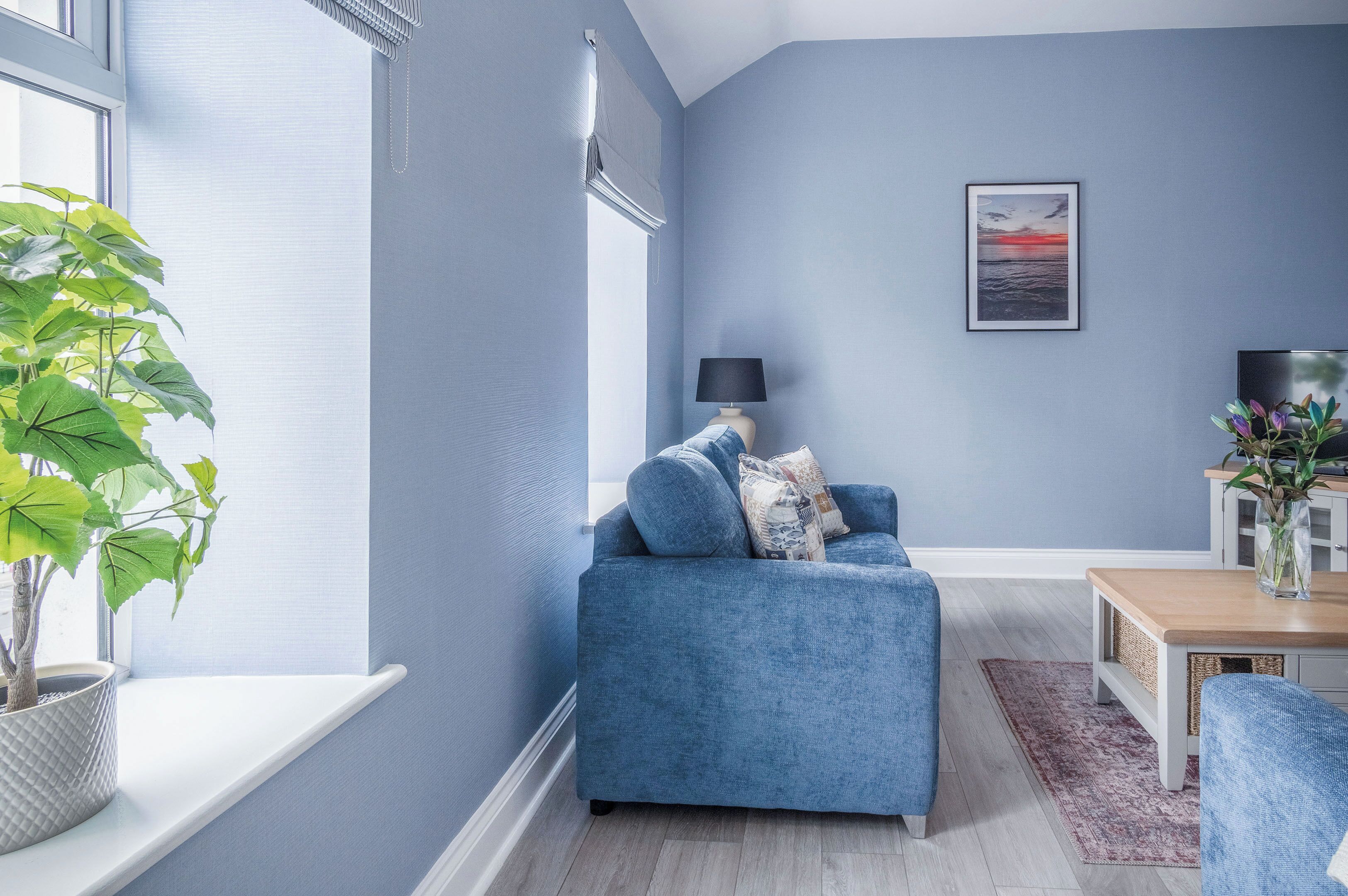 A living room with a blue sofa, a small table, a lamp, and a potted plant.