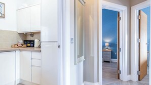 A modern kitchen with white cabinets, a coffee machine, and a small table with a lamp. - Harbour Heights - 2 Bed Apartment - Milford Haven (Milford Haven)