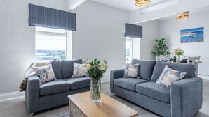 A modern living room with two grey sofas, a wooden coffee table, and a view of the city through large windows. - Beach Haven Hideout - 2 Bedroom - Milford Haven (Milford Haven)