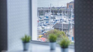 A marina with multiple boats docked, viewed through a window with potted plants on the windowsill. - Beach Haven Hideout - 2 Bedroom - Milford Haven (Milford Haven)