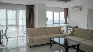 A modern living room with a beige sectional sofa, a glass coffee table, and a view of the sea through large windows. - One Tower apartments by Apartwell (Pattaya)