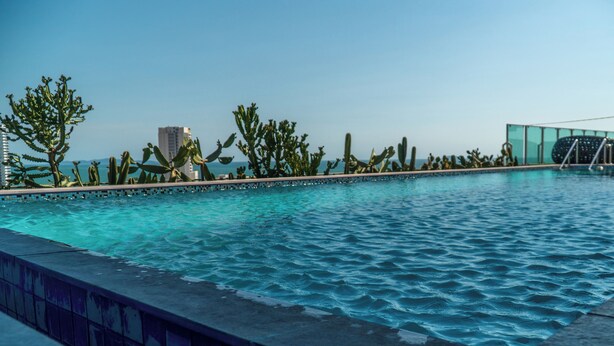 A swimming pool with a tiled edge, surrounded by cacti and a modern building in the background. - One Tower apartments by Apartwell (Pattaya)