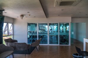 A modern gym with glass walls, wooden flooring, and contemporary chairs. - One Tower apartments by Apartwell (Pattaya)