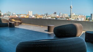 A rooftop terrace with modern wicker furniture, a city skyline in the background, and a prominent tower. - One Tower apartments by Apartwell (Pattaya)