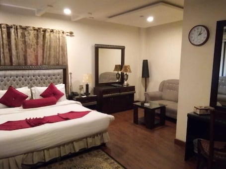 A hotel room with a large bed, a sofa, a desk, and a mirror.
