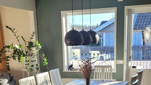 Un espace repas avec une table et des chaises en bois, un luminaire suspendu et une vue sur l’extérieur par une fenêtre.
