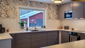 Une cuisine moderne avec des meubles gris, une grande fenêtre et une vue sur une grange rouge.
