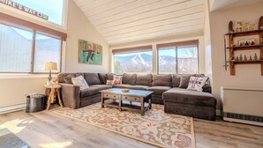 A cozy living room with a sectional sofa, a coffee table, and a large window with a view of a mountain. - Loon Mountain View at Ravine (Lincoln)