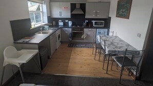 Een compacte keuken met een wasmachine, magnetron en fornuis. Er is een klein eethoekje met een tafel en stoelen.