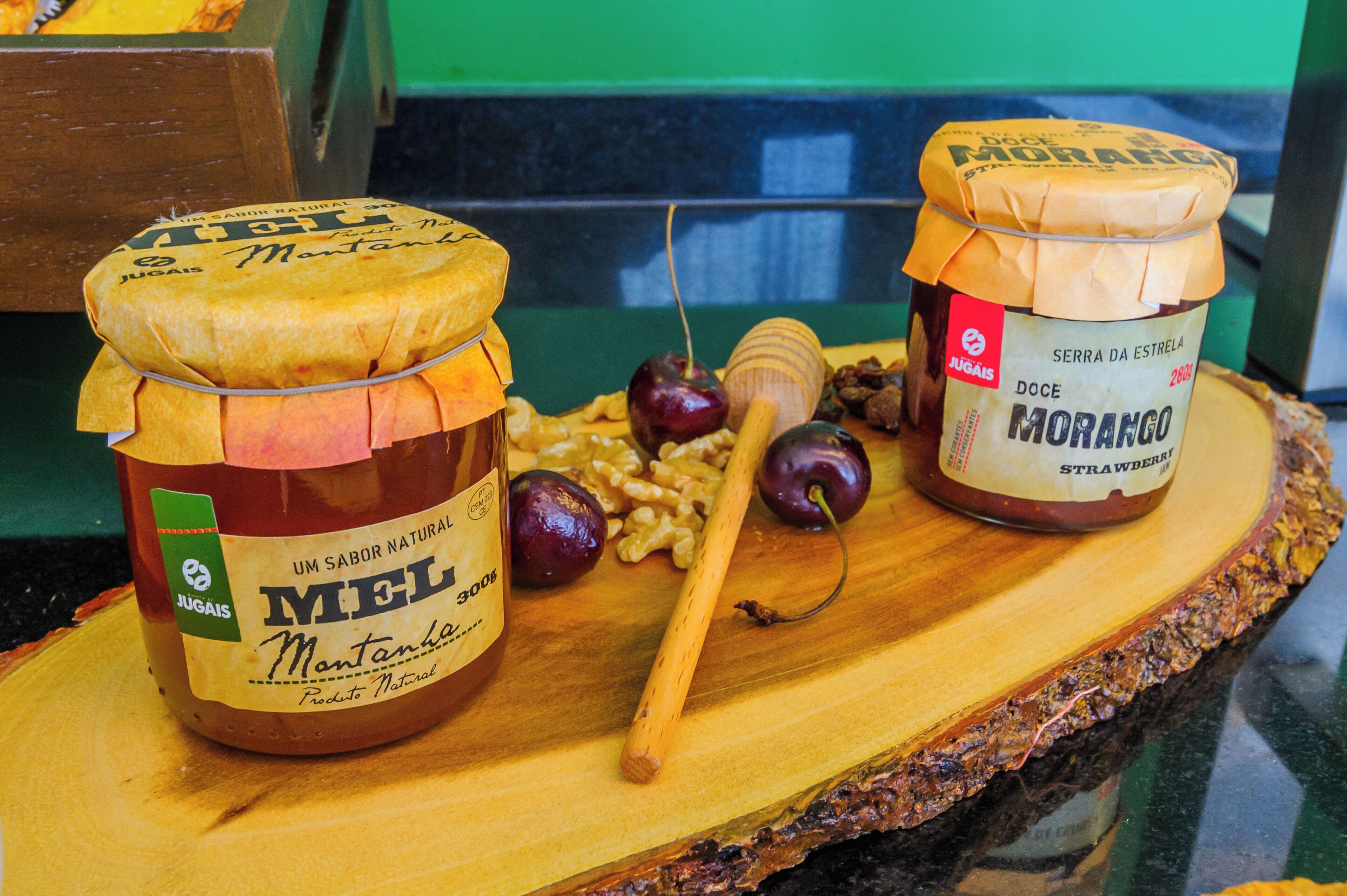 Two jars of honey on a wooden board with a honey dipper and some fruits.
