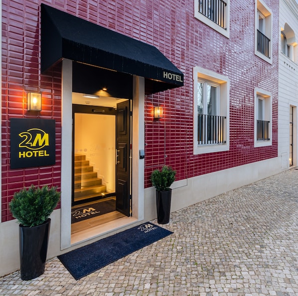 A hotel entrance with a red tiled facade, a black awning, and a sign that reads "2M HOTEL". - 2M BOUTIQUE HOTEL (Montijo)