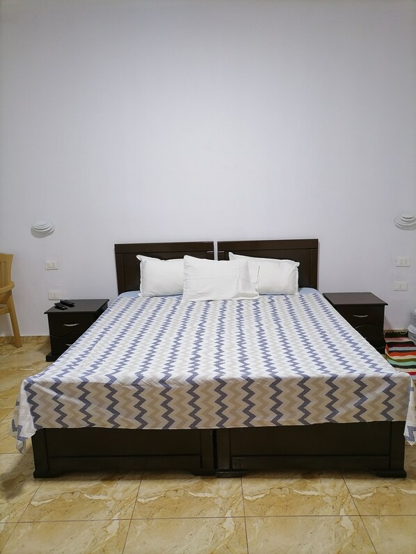 Una cama bien hecha con una colcha estampada, dos mesitas de noche y una silla.