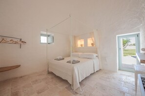 A bedroom with a four-poster bed, a small window, and a door leading to an outdoor area.
