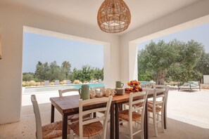 A dining area with a view of a swimming pool and trees.