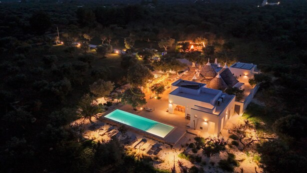 Vue aérienne d’une maison moderne dotée d’une piscine, entourée d’arbres et illuminée par des guirlandes lumineuses.