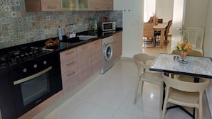 A modern kitchen with a gas stove, microwave, and washing machine. There is a dining area with a table and chairs. - Tilal Fanar Resort, Pools, Generator Included (Ain Saadeh)