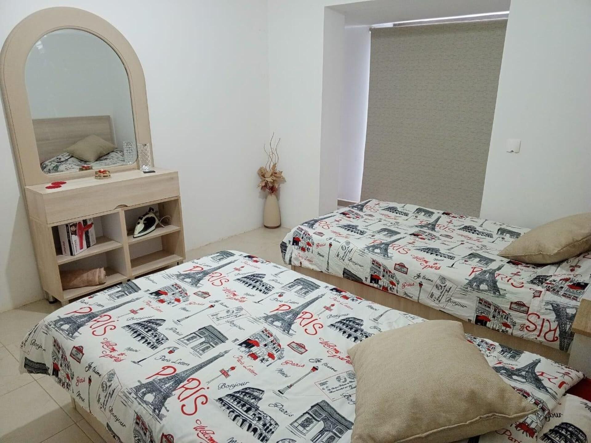 A bedroom with two beds, a dresser, a mirror, and a window with a blind.