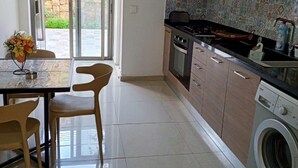 A modern kitchen with a dining area, a washing machine, and a view of a stone wall through the glass door. - Tilal Fanar Resort, Pools, Generator Included (Ain Saadeh)