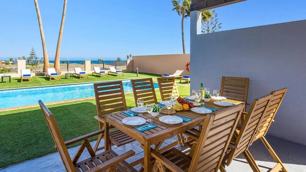 A poolside dining area with a table set for four, overlooking a pool and a beach. - Villa Humaik by Villa Plus (Antigua)