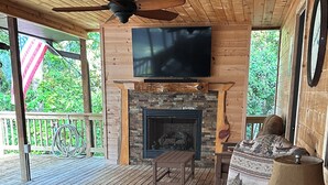 Una terraza de madera con una chimenea, un televisor montado sobre ella y asientos para exteriores.