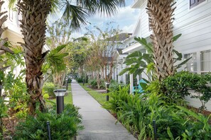 A pathway flanked by palm trees and lush greenery, leading to a row of white buildings with windows. - Beautifully Decorated Home, 10-minute drive from Disney, with Clubhouse. (Kissimmee)