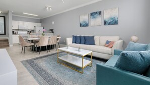 A modern living room with a white sofa, teal armchairs, a coffee table, and a dining area with chairs and a table. - Beautifully Decorated Home, 10-minute drive from Disney, with Clubhouse. (Kissimmee)