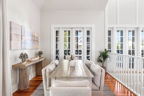 Un espace repas comprenant une table en bois, des sièges rembourrés, une console ornée d’objets décoratifs et une vue dégagée sur l’extérieur grâce à de grandes portes vitrées.