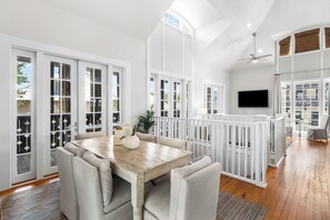 Una habitación amplia con una mesa de comedor de madera, sillas acolchadas, una barandilla blanca y un ventanal grande.