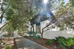 Un sendero conduce a un edificio de fachada blanca, rodeado de árboles y plantas.