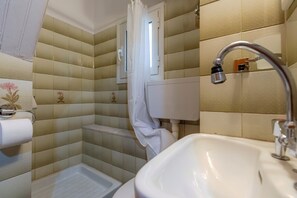Un baño con baldosas beige y blancas, un lavamanos blanco, una cortina de ducha y un inodoro.